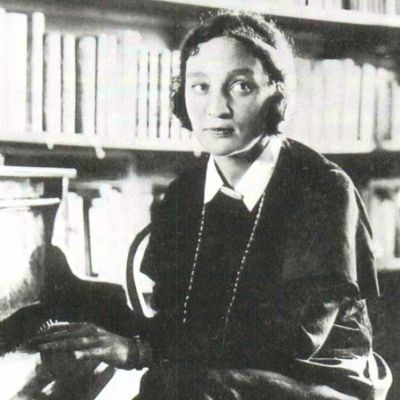 Black and white image of Maria Yudina sat next to a piano